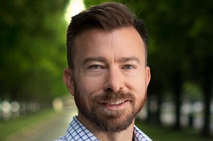 Adam Moore stands in front of a green outdoor background.