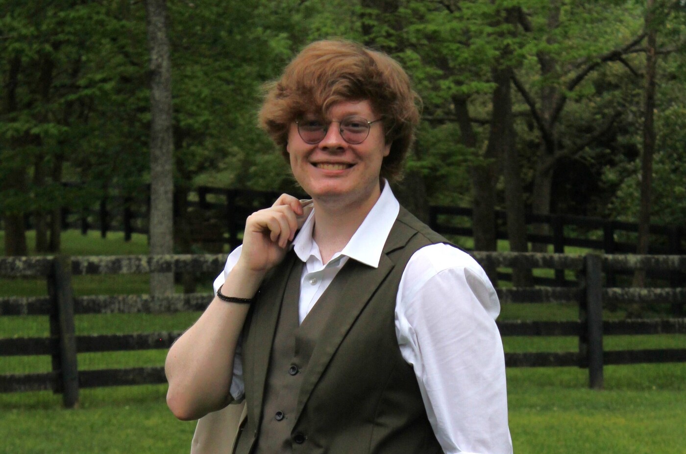 Ezra Burton poses outdoors in front of a forest and rustic fence.